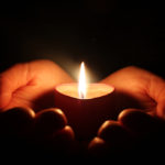 Zwei Hände, die eine brennende Kerze tragen.